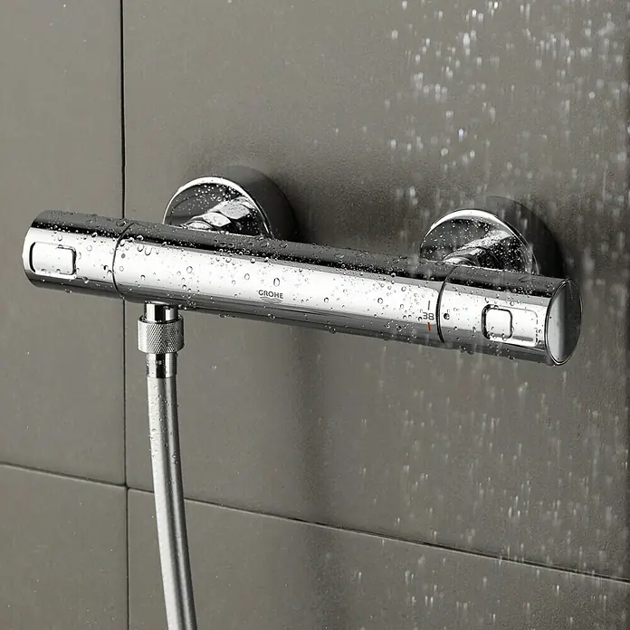 Grohe Thermostatarmatur Precision Joy - Breite: 29,9 cm, Chrom, Glänzend - Nahaufnahme einer glänzenden Grohe Duscharmatur mit Temperaturregler, montiert an einer grauen Wand mit Wassertropfen.