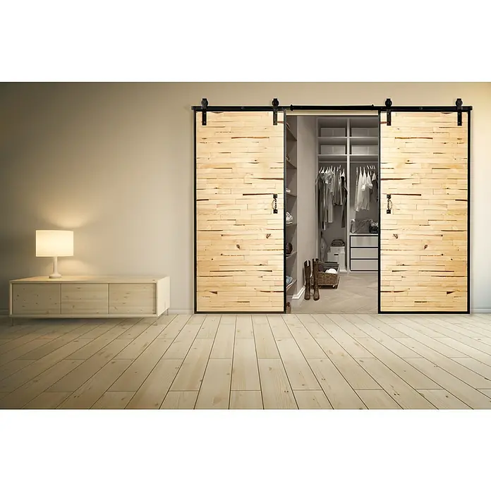 Kornik Holzschiebetür Industrial Eko - 93 x 206 cm, Kiefer - Elegante Schiebetüren aus hellem Holz mit schwarzen Beschlägen vor einem begehbaren Kleiderschrank, ergänzt durch einen passenden Schrank und eine Lampe.