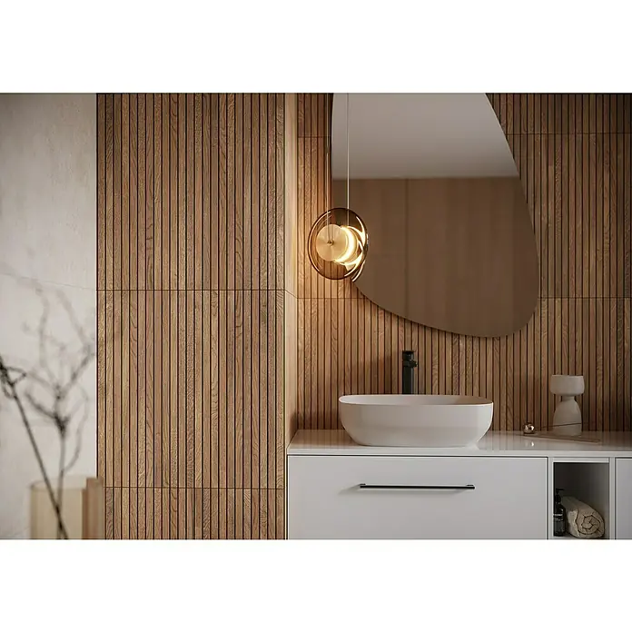 Wandfliese Boseli Wood - 29,8 x 59,8 cm, Braun, Matt - Moderne Badezimmergestaltung mit einem eleganten Waschtisch, einer stilvollen Lampe und einem asymmetrischen Spiegel vor einer Holzpaneelwand.
