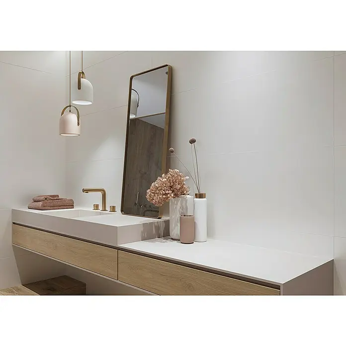 Wandfliese White Satin - 40 x 120 cm, Weiß, Matt - Ein Badezimmer-Waschtisch mit Holzschubladen, einem weißen Waschbecken und einem bronzefarbenen Wasserhahn unter modernen Pendelleuchten.