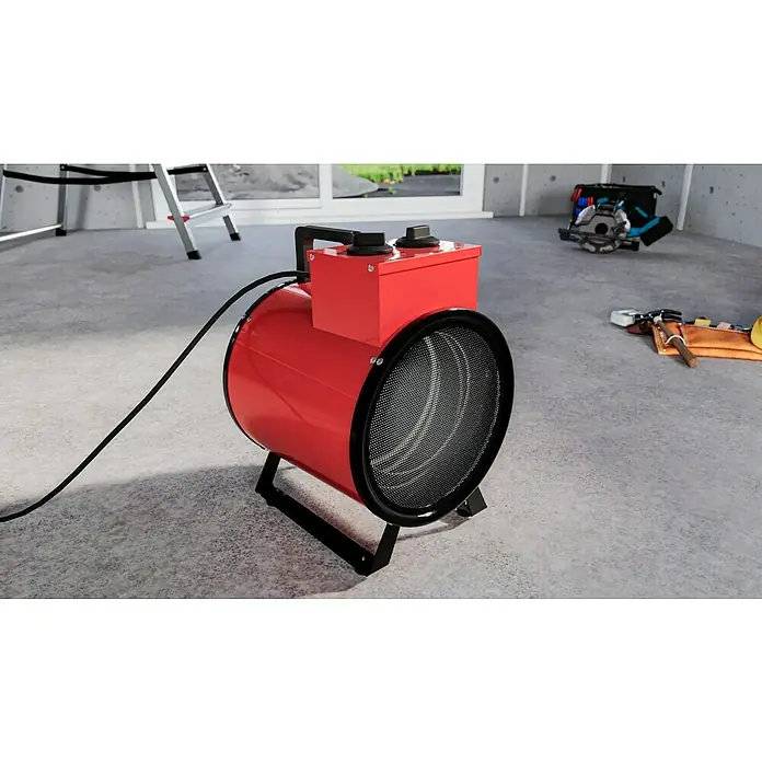 Voltomat HEATING Bauheizer - Passend für: Raumgröße bis ca. 35 m², 1.000 W - 3.000 W, Nennspannung: 220 V - 240 V, Rot, IP24 - Nahaufnahme eines roten, zylindrischen Heizlüfters mit schwarzem Gitter und Bedienelementen auf einem Betonboden in einem Raum mit Bauwerkzeugen.