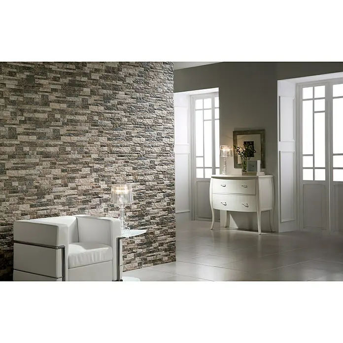 Verblendstein Durango Jet 8 - 50 x 33,3 cm, Graumix, Natursteinoptik - Elegantes Interieur mit einer Akzentwand aus Naturstein, die eine warme und einladende Atmosphäre schafft. Bequemer weißer Sessel und stilvolle Kommode.
