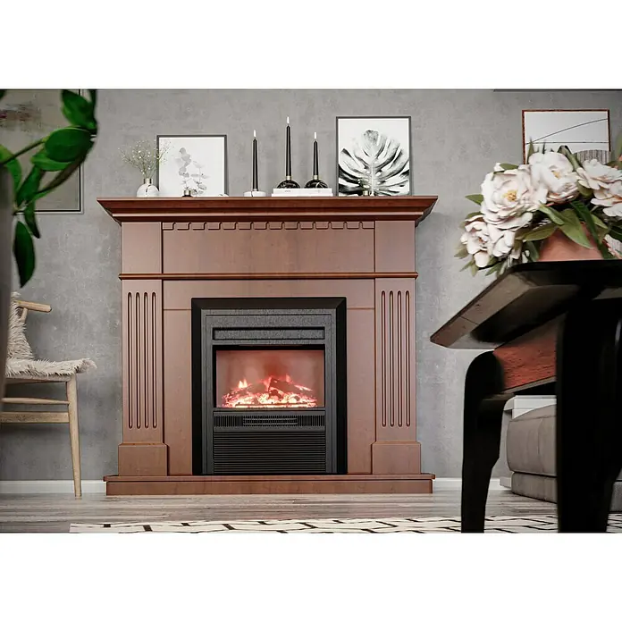 Voltomat HEATING Elektrischer Kamin - 2.000 W, Braun/Schwarz, 26 x 109 x 110 cm - Ein brauner Kamin mit schwarzem Elektroeinsatz steht vor einer grauen Wand. Dekorative Elemente wie Kerzen und Bilderrahmen schmücken den Kaminsims.