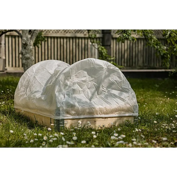 Upyard Abdeckvlies - 120 x 80 cm, Passend für: Bogen Hochbeetumrandung - Ein Frühbeetkasten mit lichtdurchlässiger Abdeckung steht auf einer grünen Wiese mit Gänseblümchen, umgeben von einem Holzzaun.