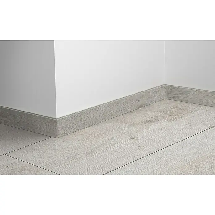 LOGOCLIC Sockelleiste Element Pro K58 C - 240 cm x 18 mm x 58 mm, Off Shore - Nahaufnahme einer grauen Holzfußleiste, die den Übergang zwischen Boden und weißer Wand elegant abschließt. Die Fußleiste fügt sich harmonisch in das Raumdesign ein.