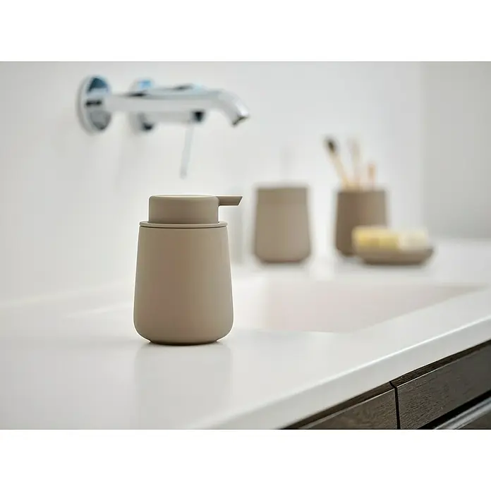 Zone Denmark Nova One Seifenschale - Keramik, Taupe - Ein beigefarbener Seifenspender aus Keramik steht auf einem weißen Waschbecken mit weiteren Badaccessoires im Hintergrund.