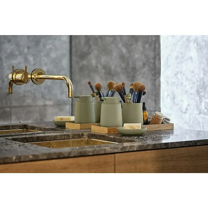 Zone Denmark Nova One Seifenschale - Porzellan, Matcha Green - Elegantes Badezimmer-Arrangement mit goldenen Armaturen, grünen Seifenspendern und Make-up-Pinseln auf einer polierten Arbeitsplatte.