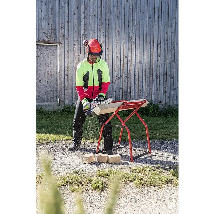 AL-KO Bosch Home & Garden Compatible Akku-Kettensäge CS 1825 - 18 V, Li-Ionen, Ohne Akku, Schwertlänge: 25 cm - Holzarbeiter mit Schutzhelm, Gesichtsschutz und Arbeitskleidung sägt mit einer AL-KO Motorsäge ein Holzstück auf einem roten Sägebock.