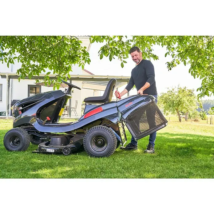 AL-KO Comfort Rasentraktor 18-103.4 HD-A V2 - 568 cm³, Schnittbreite: 103 cm - Ein Mann entleert den Fangkorb eines AL-KO Aufsitzmähers auf einem gepflegten Rasen, umgeben von üppigem Grün und einem modernen Haus im Hintergrund.