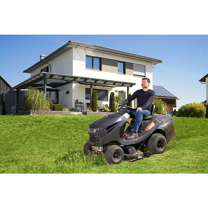 AL-KO Comfort Rasentraktor 18-103.4 HD-A V2 - 568 cm³, Schnittbreite: 103 cm - Ein Mann sitzt auf einem AL-KO Aufsitzmäher und mäht den Rasen vor einem modernen Haus mit Solaranlagen.