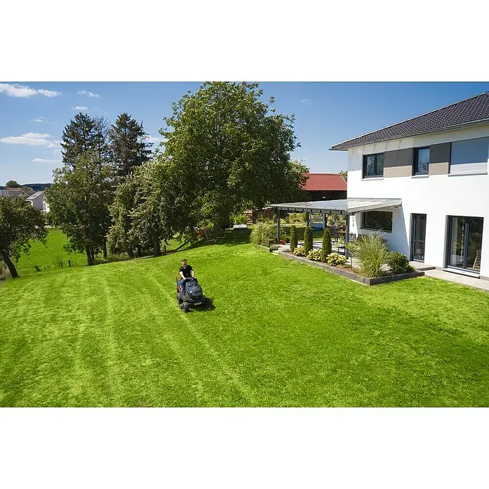 AL-KO Comfort Rasentraktor 18-103.4 HD-A V2 - 568 cm³, Schnittbreite: 103 cm - Ein Mann mäht den Rasen mit einem Rasenmäher in einem großen Garten. Das Haus und der gepflegte Garten ergänzen das Bild.