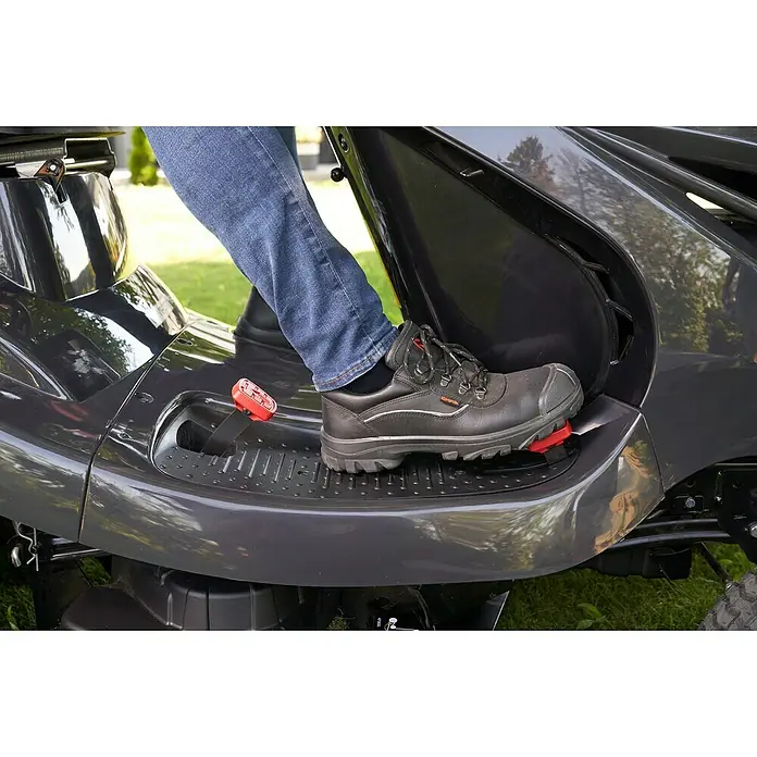 AL-KO Comfort Rasentraktor 18-111.4 HDS-A V2 - 568 cm³, Schnittbreite: 110 cm - Ein Fuß in einem robusten Sicherheitsschuh ruht auf der Trittfläche eines Rasentraktors, der für sicheres Auf- und Absteigen konzipiert ist.