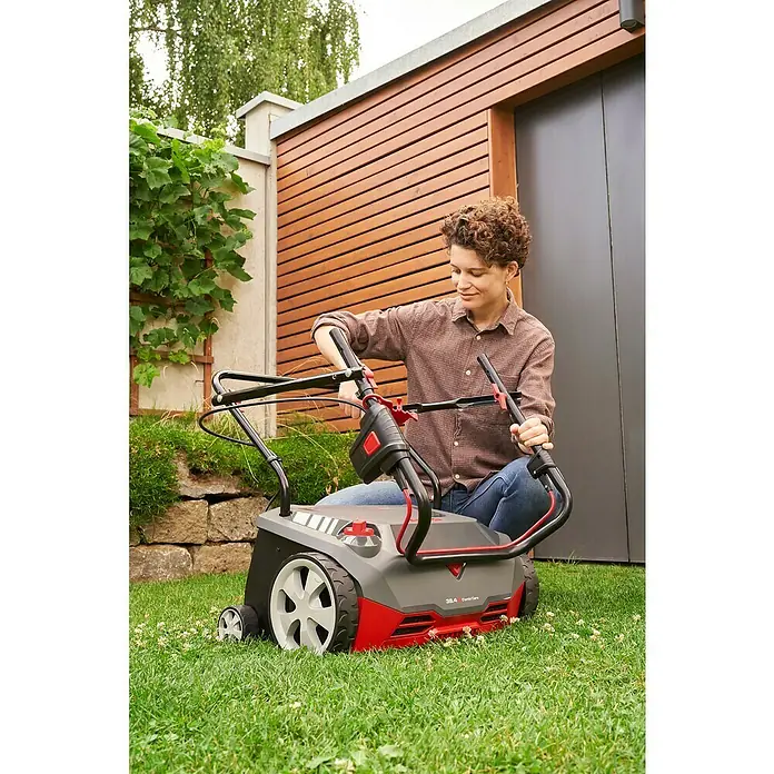 AL-KO Easy Elektro-Vertikutierer-Lüfter 38.4 E Combi Care - 1.400 W, Arbeitsbreite: 38 cm - Eine Frau bedient einen Rasenlüfter im Garten. Das Gerät ist rot und grau und steht auf einer grünen Rasenfläche.