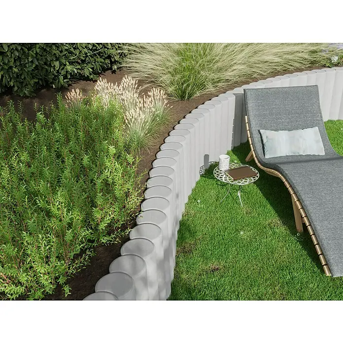 Diephaus Rundpalisade - Ø x H: 20 x 100 cm, Grau, Beton - Nahaufnahme einer dekorativen Betonmauer, die einen Gartenbereich mit grünen Pflanzen und einem Liegestuhl im Freien abgrenzt.