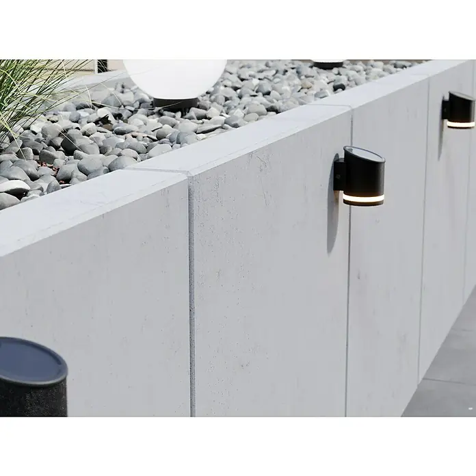 Diephaus L-SteinBewehrt, Höhe: 105 cm, Breite: 100 cm, Stärke: 12 cm, Grau - Eine graue Betonmauer mit schwarzen, zylinderförmigen Lampen. Die Lampen werfen ein warmes Licht auf die Mauer und erhellen den Bereich.