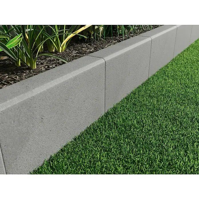 Diephaus L-Stein - 30 cm, 50 cm, Stärke: 7 cm, Grau - Nahaufnahme einer Rasenkante aus Betonsteinen, die einen Gartenbereich stilvoll abgrenzt. Die Steine haben eine graue Farbe und eine leicht raue Oberfläche.