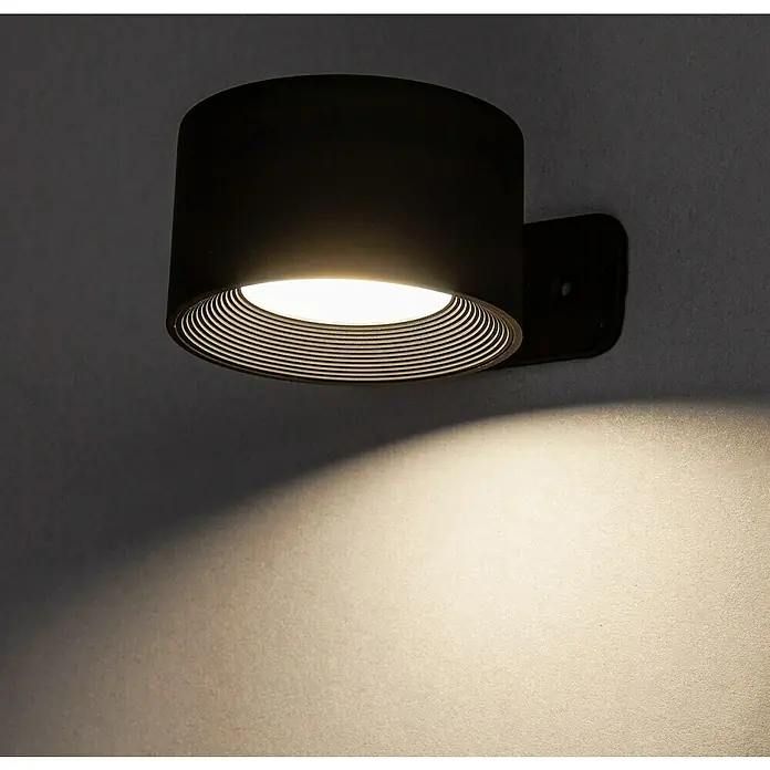 Lavida Akku-Wandleuchte Novara - L x B x H: 9,25 x 7,6 x 4,5 cm, 2 W, Schwarz, Mehrfarbig, Rund - Nahaufnahme einer schwarzen zylindrischen Wandleuchte, die warmes Licht auf eine Wand wirft.