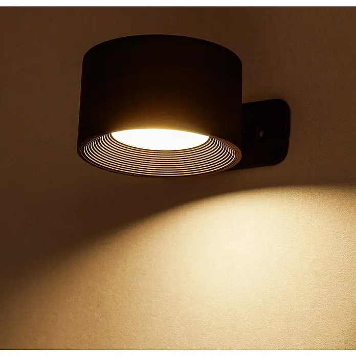 Lavida Akku-Wandleuchte Novara - L x B x H: 9,25 x 7,6 x 4,5 cm, 2 W, Schwarz, Mehrfarbig, Rund - Nahaufnahme einer modernen, zylindrischen Wandleuchte in Schwarz mit warmweißem Licht, die einen dekorativen Lichtkegel an die Wand wirft.