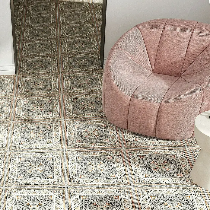 Steingutfliese Colonial - 45 x 45 cm, Beige, Glänzend - Nahaufnahme von Bodenfliesen mit einem komplizierten, wiederholenden Muster und einem rosafarbenen Sessel, der ein gemütliches Ambiente schafft.