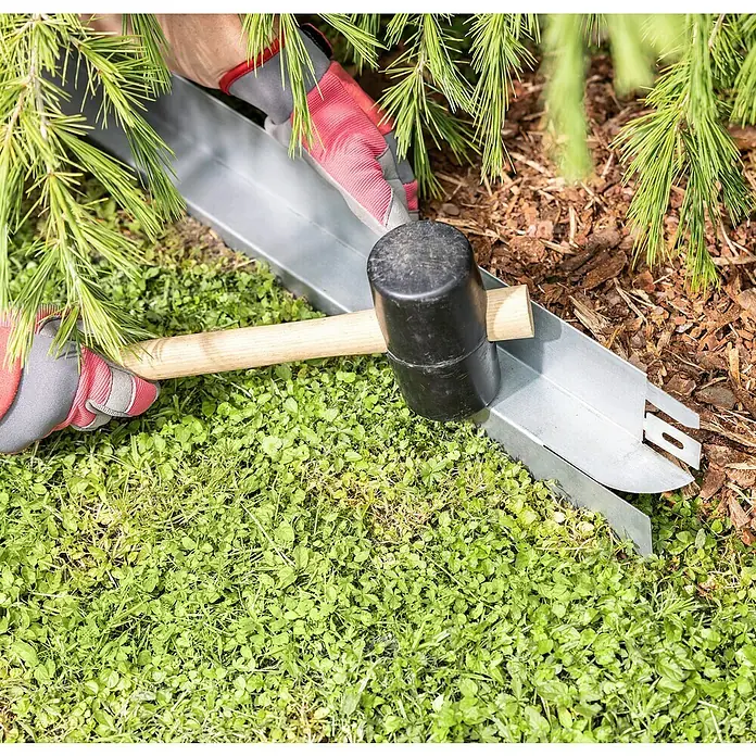 Windhager Rasenkante Easycut - L x B x H: 80 x 0,4 x 11 cm, Stahl, Verzinkt - Ein Gartenarbeiter installiert mit einem Gummihammer eine Rasenkante aus Metall, um einen sauberen Übergang zum Blumenbeet zu schaffen.