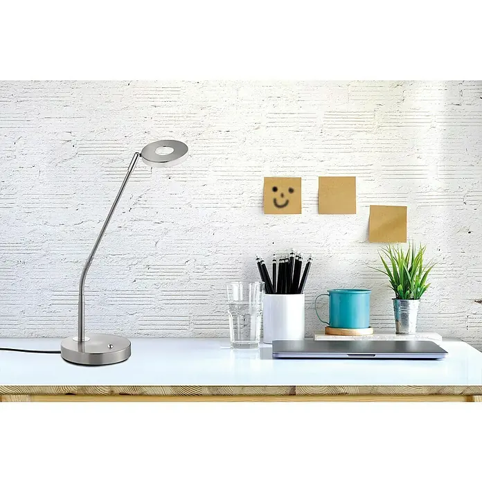 Fischer & Honsel Dent LED-Tischleuchte - 6 W, L x B x H: 40 x 16 x 60 cm, Nickel matt, Warmweiß - Schreibtisch mit einer modernen, runden LED-Lampe, Stiften, Tasse, Pflanze und Haftnotizen vor einer weißen Ziegelwand.