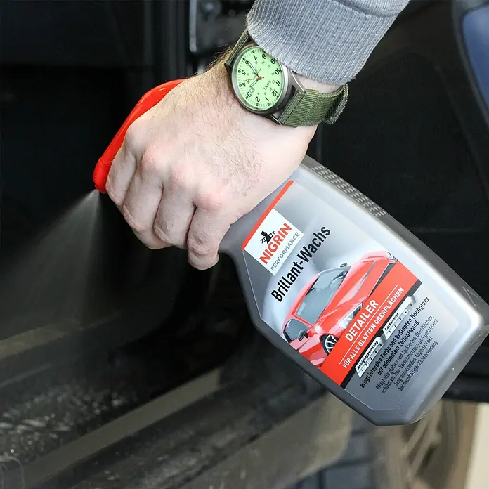 Nigrin Performance Wachspolitur Brillant Wachs Turbo - 500 ml - Detailaufnahme einer Person, die Nigrin Brillant-Wachs Detailer auf eine Autooberfläche sprüht, um Glanz und Schutz zu gewährleisten.