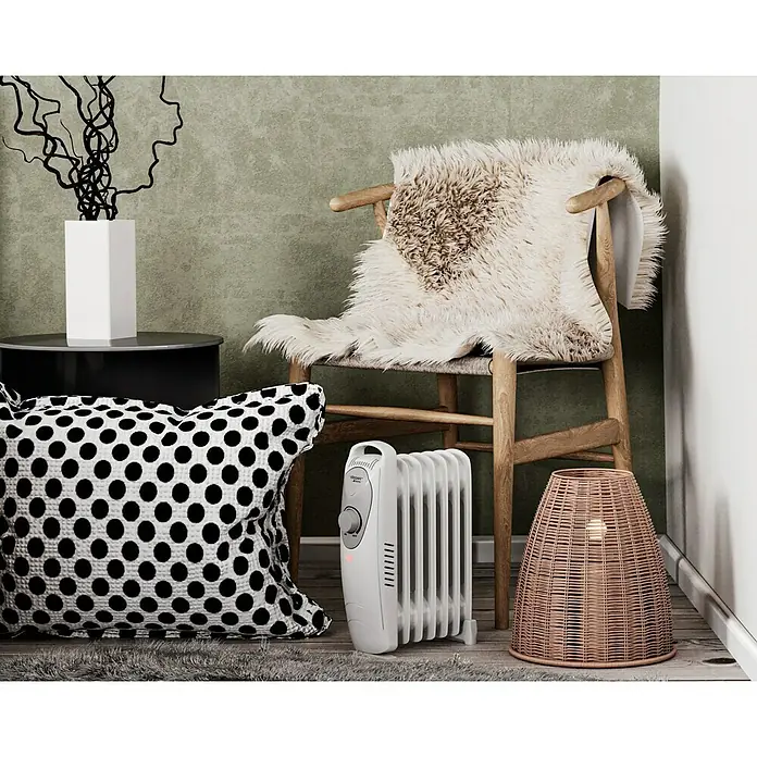Voltomat HEATING Radiador de aceite Mini - 800 W, Habitaciones hasta 8 m², Blanco - Primer plano de un radiador de aceite blanco junto a una lámpara de mimbre, una silla con una manta de piel y un cojín.