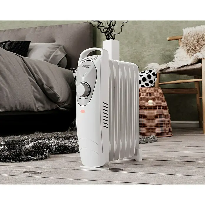 Voltomat HEATING Radiador de aceite Mini - 800 W, Habitaciones hasta 8 m², Blanco - Un radiador de aceite blanco sobre un piso de madera frente a una cama y una silla, para calor y confort.