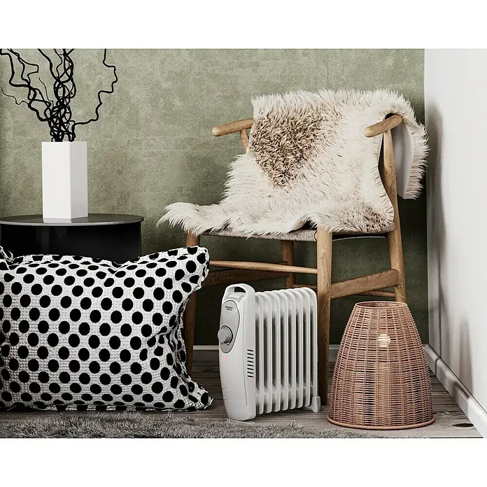 Voltomat HEATING Radiador de aceite Mini - 1.000 W, Habitaciones hasta 10 m², Blanco - Un calefactor portátil junto a una silla de mimbre con una manta de piel y un cojín. Ideal para calor adicional.