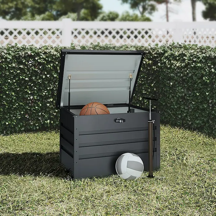 Hoggar Garten-Aufbewahrungsbox Sveg - L x B x H: 61 x 72 x 63 cm, Anthrazit, Metall - Bild eines grauen Auflagendeckels mit Basketball und Volleyball im Garten.