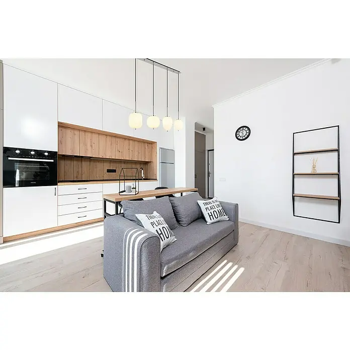 Globo LED-Pendelleuchte Blacky I - 40 W, Anzahl Leuchtmittel: 4 Stk., L x B x H: 110 x 18,5 x 120 cm, E14, Weiß - Helle Wohnungseinrichtung mit einer grauen Couch mit Kissen und einer Küchenzeile im Hintergrund, die ein gemütliches Wohnambiente schafft.
