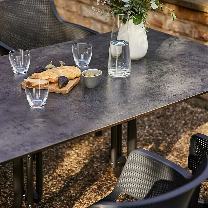 Siena Garden Gartentisch Sola - L x B x H: 160 x 90 x 71 cm, Stahl, HPL, Rechteckig, Anthrazit - Ein stilvoller Esstisch aus dunklem Material mit Speisen und Getränken im Freien, umgeben von modernen Stühlen.
