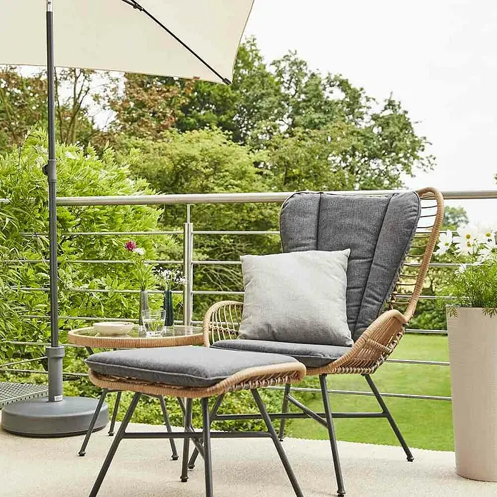 Siena Garden Marktschirm City Push - Natur, Bespannungsmaß (L x B): 180 x 180 cm - Gartenmöbel-Set mit Rattansessel, Fußhocker und Beistelltisch unter einem Sonnenschirm auf einer Terrasse mit Pflanzen und Bäumen.