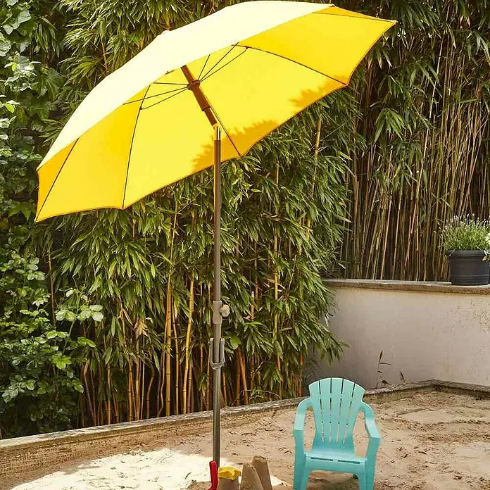 Siena Garden Marktschirm rund City Push - Gelb, Durchmesser Bespannung: 180 cm - Ein gelber Sonnenschirm spendet Schatten über einem Sandkasten mit einem blauen Stuhl und Sandspielzeug im Garten.