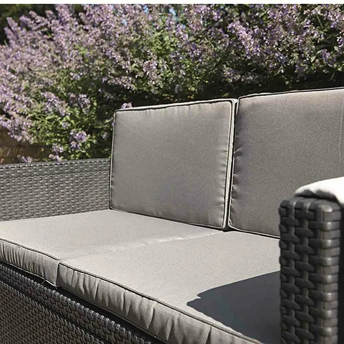Allibert Loungemöbel-Set Monaco - 4 -tlg., Kunststoffgeflecht, Polyester, Graphit - Nahaufnahme eines grauen Gartensofas mit Kissen vor blühenden Pflanzen. Das Sofa lädt zum Entspannen im Freien ein.