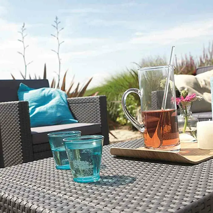 Allibert Loungemöbel-Set Monaco - 4 -tlg., Kunststoffgeflecht, Polyester, Graphit - Einrichtungsidee für den Außenbereich mit zwei blauen Gläsern und einem Getränkekrug auf einem grauen Rattantisch.
