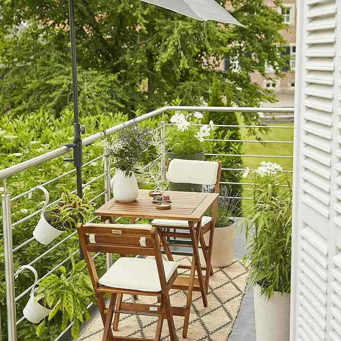 Siena Garden Balkonschirm City Push - Anthrazit, Bespannungsmaß (L x B): 160 x 100 cm - Ein quadratischer Holztisch mit zwei Stühlen und beigen Polstern steht auf einem Balkon mit Pflanzen und einem Sonnenschirm.