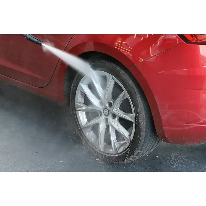 Nigrin Felgenreiniger - 1 l - Nahaufnahme eines roten Autos, dessen Rad mit einem Hochdruckreiniger gewaschen wird, um Schmutz und Ablagerungen zu entfernen.