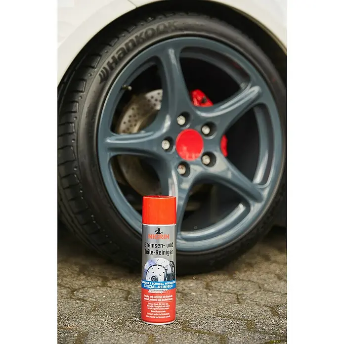 Nigrin Bremsen- & Teilereiniger - 500 ml - Das Bild zeigt eine Dose NIGRIN Bremsen- und Teile-Reiniger vor einem Autorad, das professionelle Reinigung und Pflege verspricht.