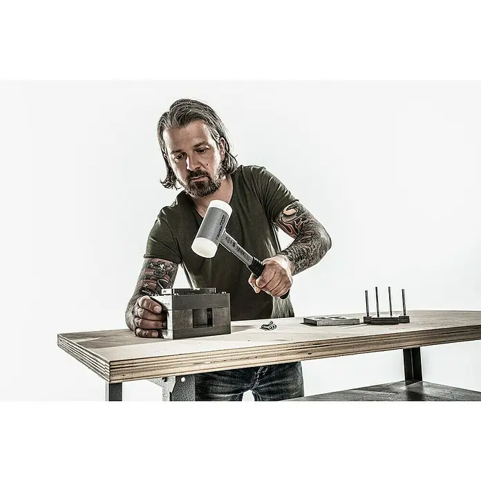 Halder Supercraft Schonhammer - Durchmesser Kopf: 50 mm, Hart - Ein Mann bearbeitet ein Metallstück mit einem SIMPLEX Schonhammer auf einer Werkbank. Das Werkzeug ist robust und vielseitig einsetzbar.