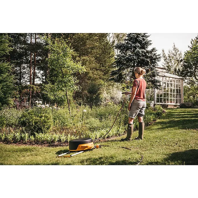 Fiskars X-series Automatische Schlauchtrommel XL mit Rädern - Schlauchlänge: 25 m - Eine Frau gießt ihren Garten mit einer Fiskars Gießanlage. Der Aufroller ist orange und schwarz.