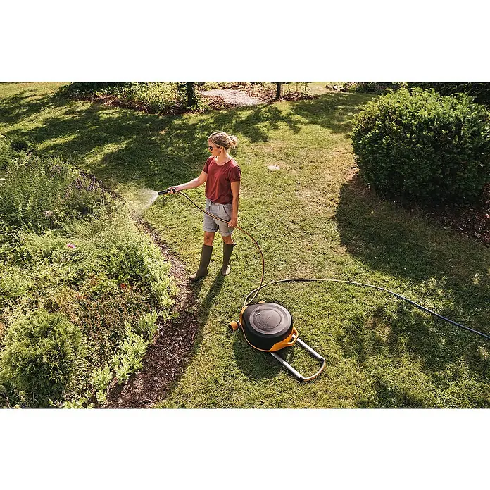 Fiskars X-series Automatische Schlauchtrommel XL mit Rädern - Schlauchlänge: 25 m - Frau gießt Garten mit Fiskars Schlauchwagen. Praktisch und effizient für die Gartenbewässerung mit hoher Reichweite.