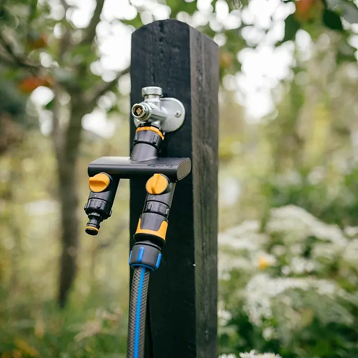 Fiskars 2-Wege-Ventil - Ø 21 mm (G 1/2"), Ø 26,5 mm (G 3/4") und Ø 33,3 mm (G 1") - Nahaufnahme eines Fiskars-Wasserverteilers am Wasserhahn mit einem Schlauch angeschlossen, im Garten.