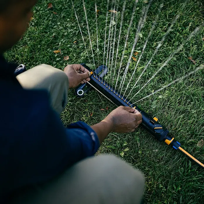 Fiskars X-series Ersatzteil-Set - Max. Regnerfläche: 300 m² - Mann justiert einen Fiskars Oszillationsregner auf einer grünen Rasenfläche, um die Bewässerung anzupassen. Optimale Gartenbewässerung.