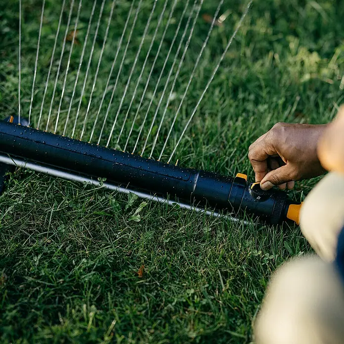 Fiskars X-series Ersatzteil-Set - Max. Regnerfläche: 350 m², Passend für: Größere Flächen - Eine Person bedient einen Rasensprenger auf einem grünen Rasen, um die Bewässerung einzustellen.
