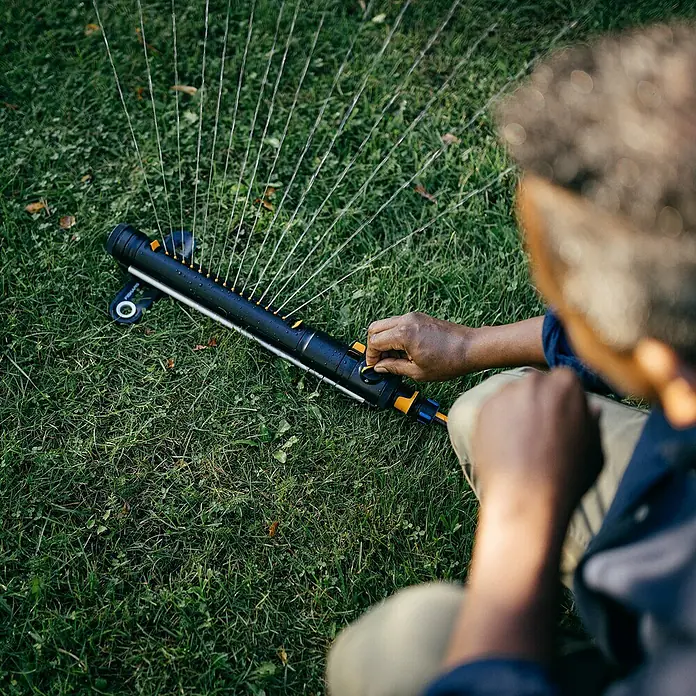 Fiskars X-series Ersatzteil-Set - Max. Regnerfläche: 300 m² - Ein Mann bedient einen Fiskars Rechteckregner auf einem grünen Rasen, der das Gras mit Wasser versorgt.