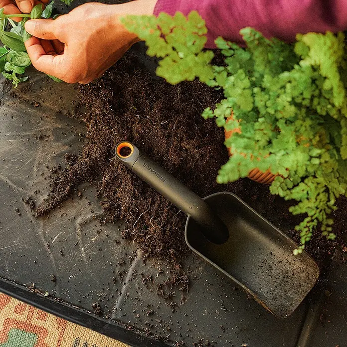 Fiskars Pflanzkelle - 29,1 cm - Nahaufnahme eines Fiskars Pflanzschaufel auf einer Pflanzmatte, umgeben von Erde und Pflanzen, ideal für Gartenarbeiten.