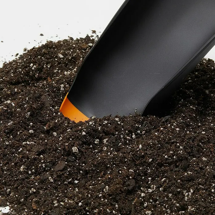 Fiskars Kehrschaufel-Set - Kunststoff - Nahaufnahme eines schwarzen Gartenschaufel, die in dunkle Erde gesteckt wird. Die Schaufel hat eine orangefarbene Spitze.