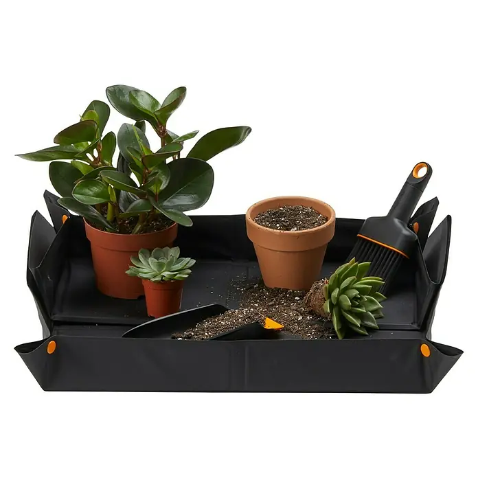 Fiskars Kehrschaufel-Set - Kunststoff - Gartenszene mit einer schwarzen Pflanzmatte, Töpfen, Sukkulenten und Gartengeräten, die eine saubere und organisierte Bepflanzung ermöglicht.