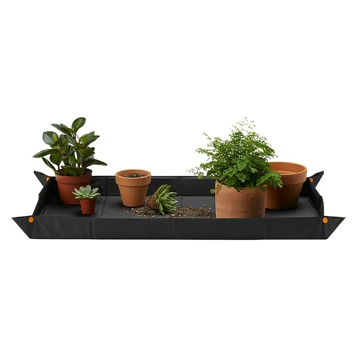 Fiskars Pflanzmatte - 96,8 x 57,8 cm - Das Bild zeigt eine Pflanzmatte mit verschiedenen Pflanzen und Töpfen darauf, ideal für Hobbygärtner, um sauber zu arbeiten.